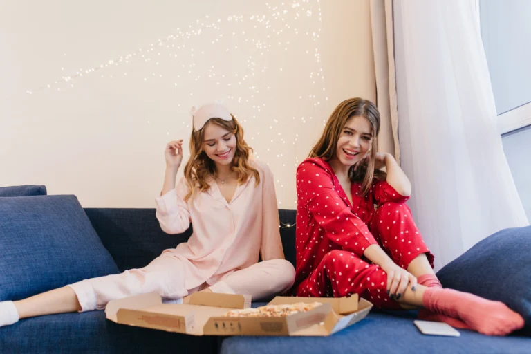 carefree-girls-cute-night-suits-eating-pizza-together-romantic-young-woman-red-pajama-sitting-sofa-with-sister-enjoying-fast-food